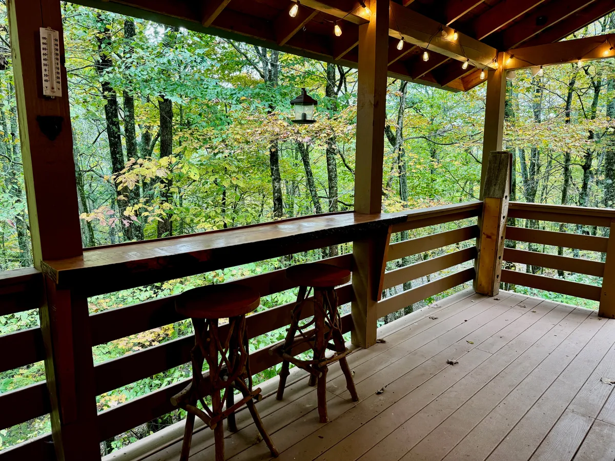 A tranquil deck scene with a bar counter and stools, surrounded by towering trees and illuminated by hanging lanterns. The setup encourages sipping morning coffee or evening drinks while soaking in the sights and sounds of the forest.