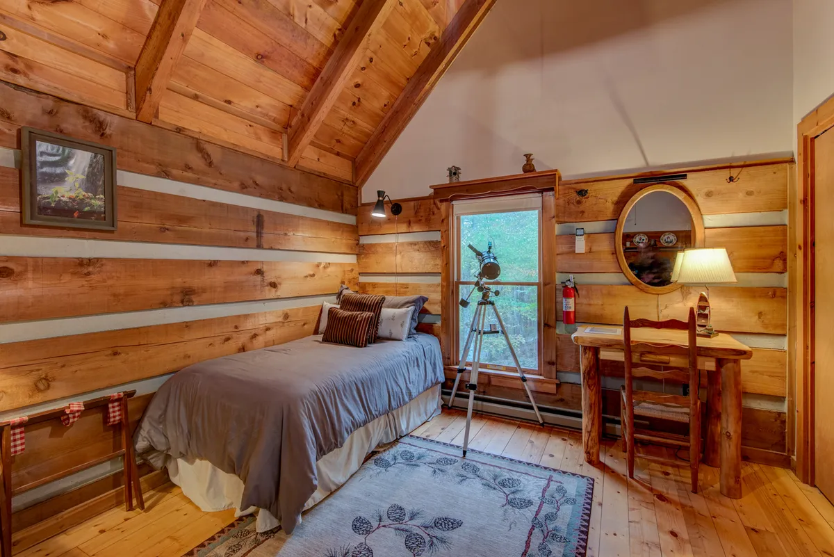A wooden bed is paired with a telescope, decorative mirror, and a side table with a lamp. The peaceful room offers a reflective atmosphere and a touch of whimsy, inviting guests to stargaze or enjoy a quiet evening.