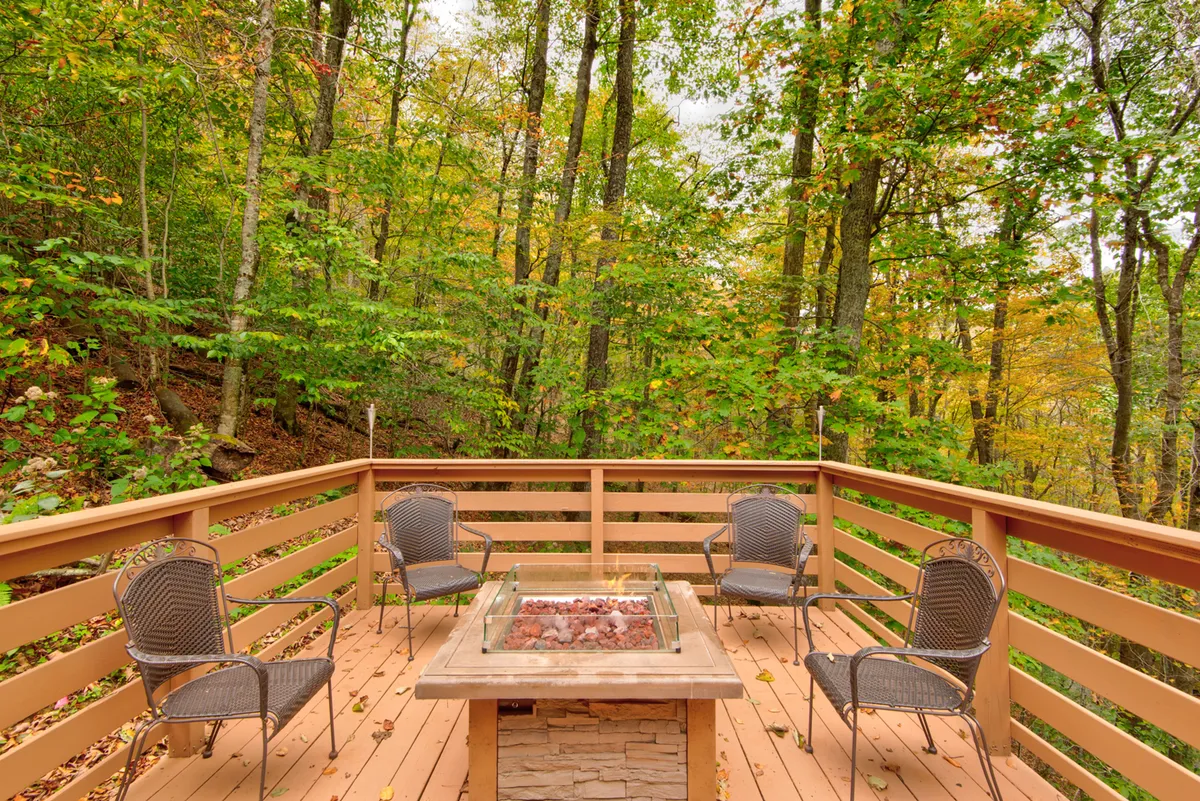 A welcoming fire pit is surrounded by comfortable deck seating, set against a backdrop of tall trees. The area invites families or friends to gather in the evening, toasting marshmallows or sharing stories under the open sky. The overall mood is peaceful and inviting, with hints of sunset light filtering through the trees.