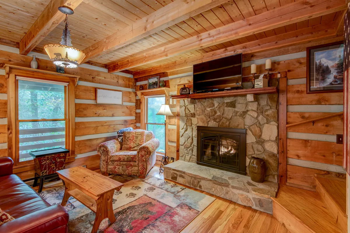 This inviting shot focuses on a comfortable armchair set by a grand stone fireplace, with natural light streaming in from large windows. The wooden coffee table and ample space hint at both intimate and group gatherings, while the warm, welcoming mood matches the section's narrative of togetherness and comfort.