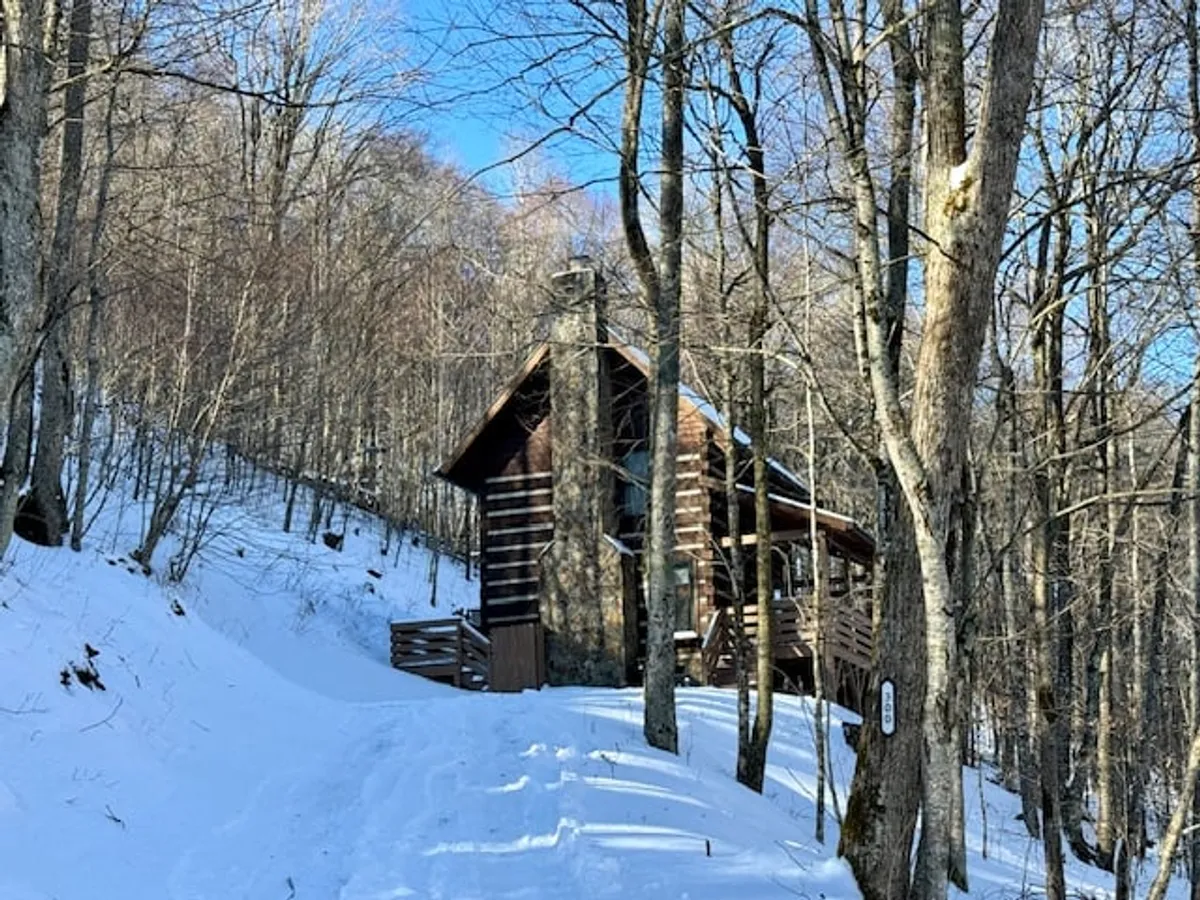 A peaceful exterior shot of the Casa Haven log cabin nestled among snow-covered trees, with a snowy path leading towards the entrance. The scene captures the quiet stillness of winter and hints at the kind of snowy adventures and cozy nights described in the section.