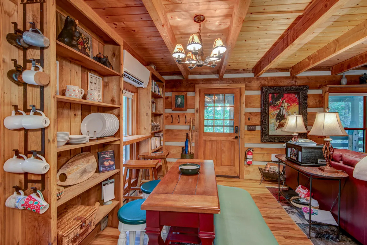 A bright dining area with a large wooden table, a striking chandelier, shelves filled with dishware, and a door leading to the outdoors. The image radiates warmth and a sense of togetherness, ideal for family meals or sharing stories.
