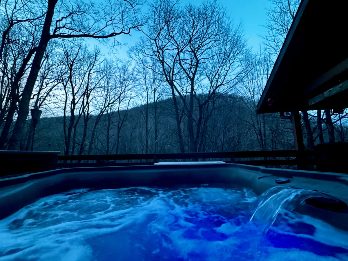 A serene outdoor scene featuring a private hot tub set against a backdrop of mountain views and lush trees. The hot tub sits on a wooden deck, inviting relaxation and intimate moments under the open sky, perfect for unwinding after a day of exploration.